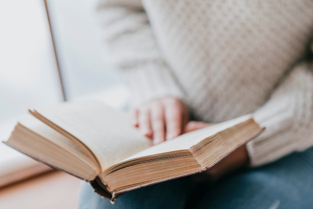 Crop woman enjoying reading near window