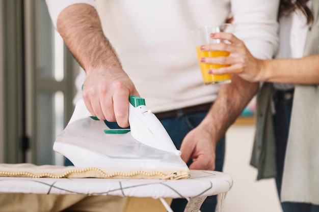 Crop woman giving juice to ironing man