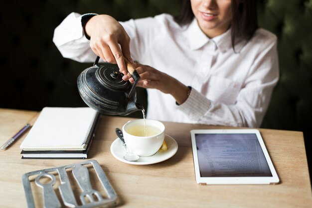 Crop woman having tea while studying