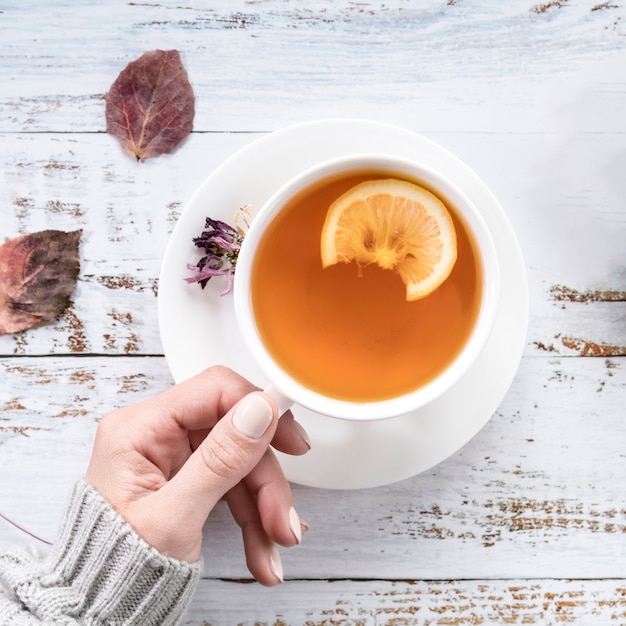 Crop woman holding cup of tea on shabby surface