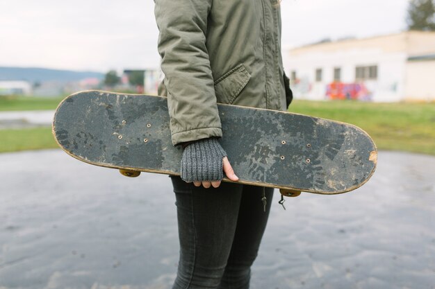 汚れたスケートボードを保持する作物の女性