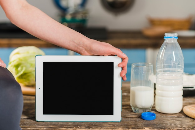 Crop woman holding tablet near milk
