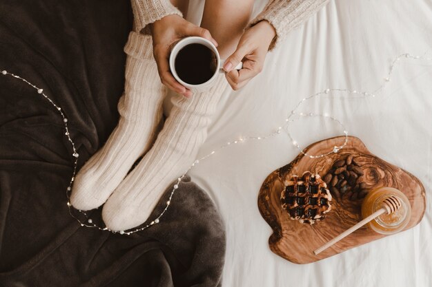 Crop woman holding tea near snacks