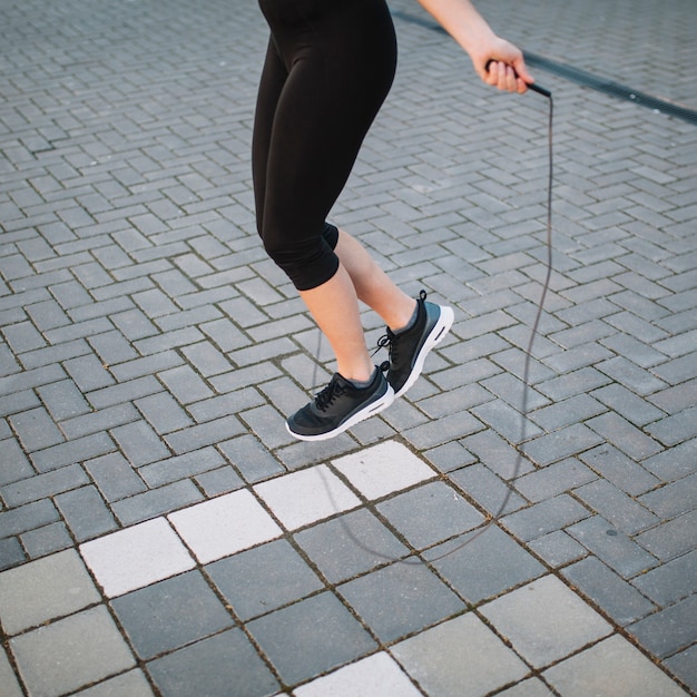 Crop woman jumping with rope on street
