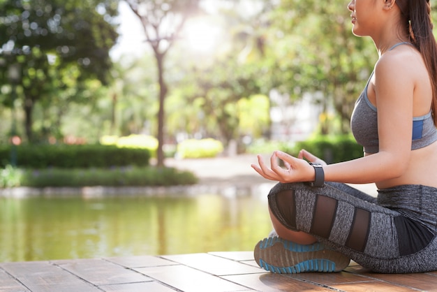 Crop woman meditating in green summer park