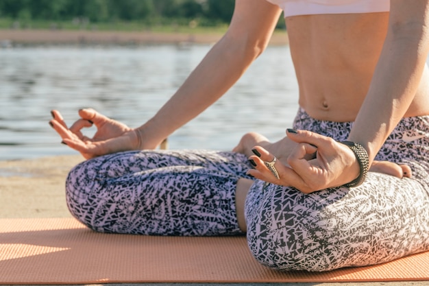 Crop woman meditating at water