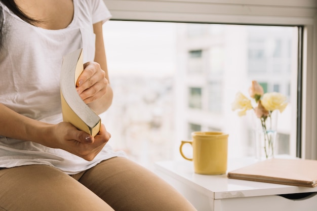 Free photo crop woman opening book near window