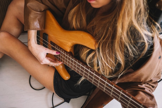 Crop woman playing guitar on floor