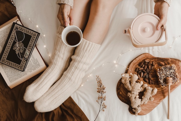 Crop woman pouring tea near books and snacks