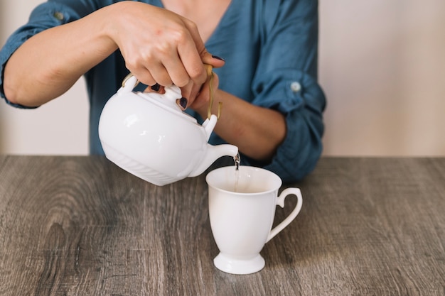 Crop woman pouring tea