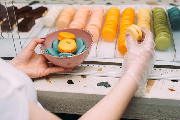 Crop woman putting macaroons in bowl