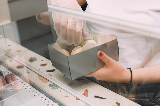 Free photo crop woman putting macaroons in box