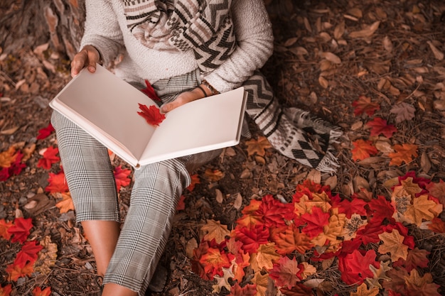 Free photo crop woman reading on autumn ground