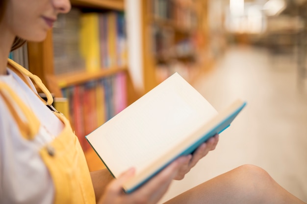 Crop woman reading book in library