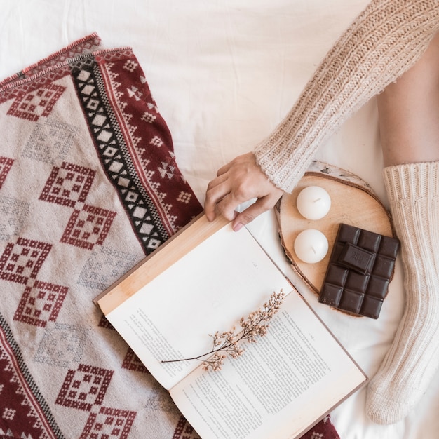 Crop woman reading book near chocolate