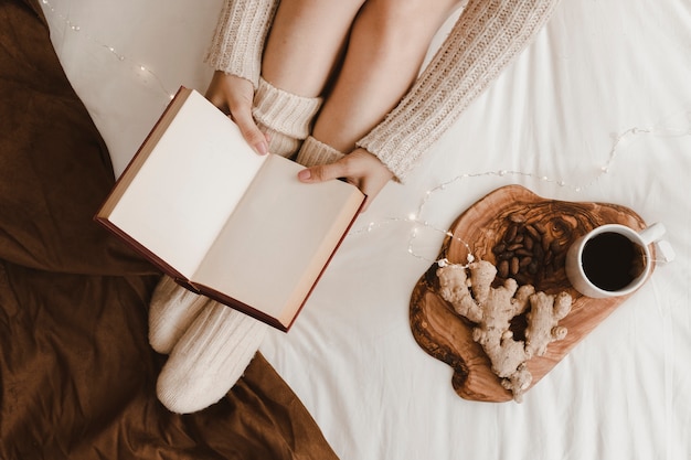 Crop woman reading near tea and ginger