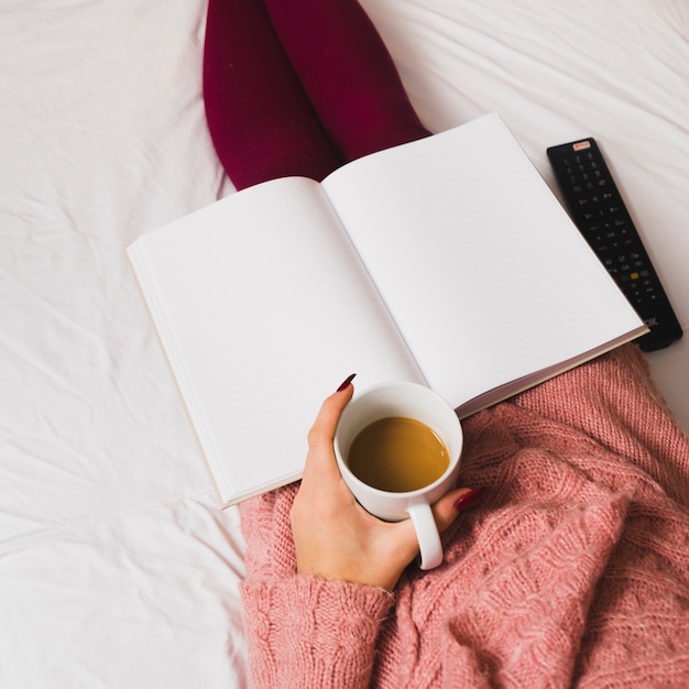 Crop woman relaxing with coffee and notebook