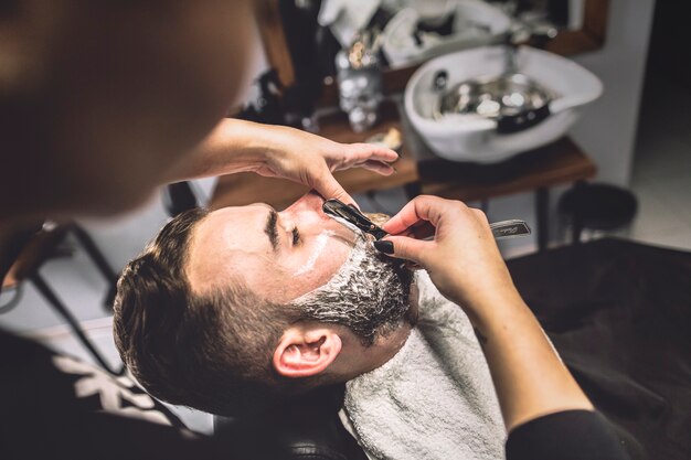 Crop woman shaving man in salon