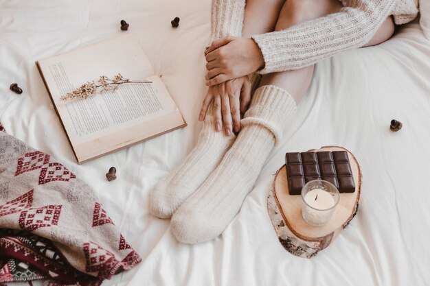 Crop woman sitting between book and chocolate