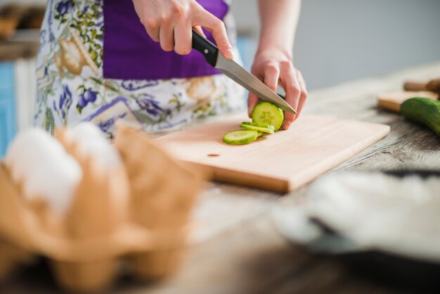 Crop woman slicing cucumber