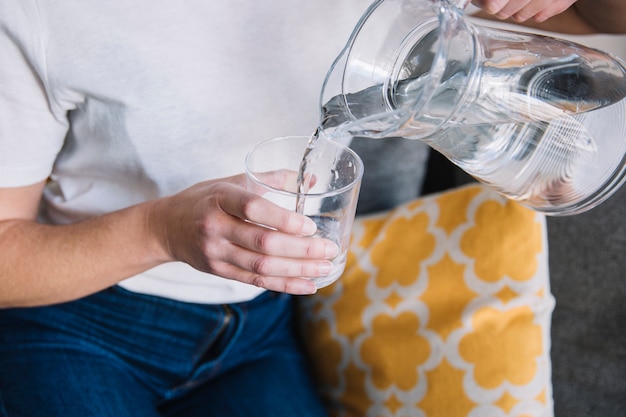 Free photo crop woman on sofa pouring water