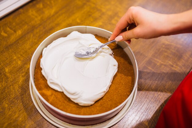 Crop woman spreading cream on cake