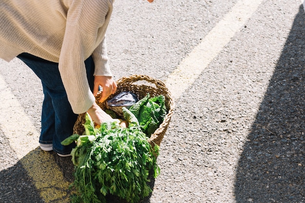 Crop woman taking vegetables from basket