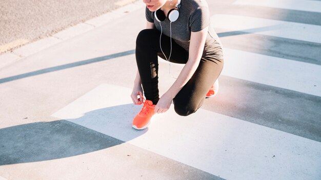 Crop woman tying laces on crosswalk