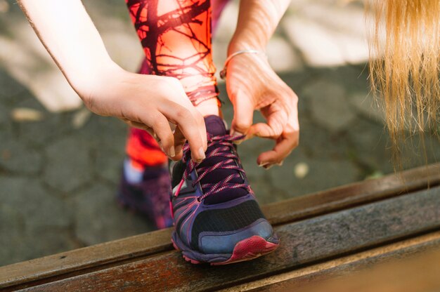 Crop woman tying laces on sneakers