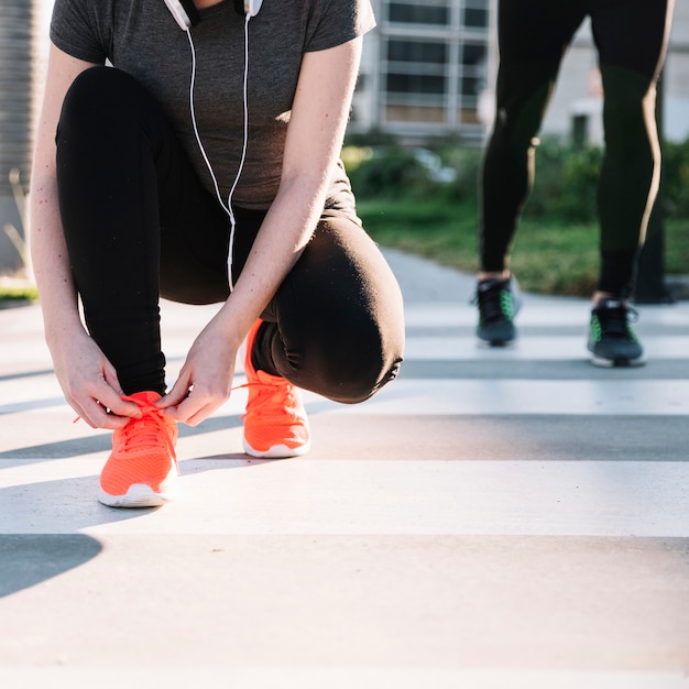 Ritaglia la donna che lega i lacci con le scarpe da ginnastica