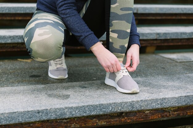 Crop woman tying laces on stairs