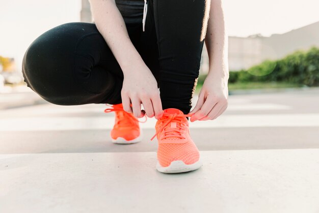 Crop woman tying peach sneakers