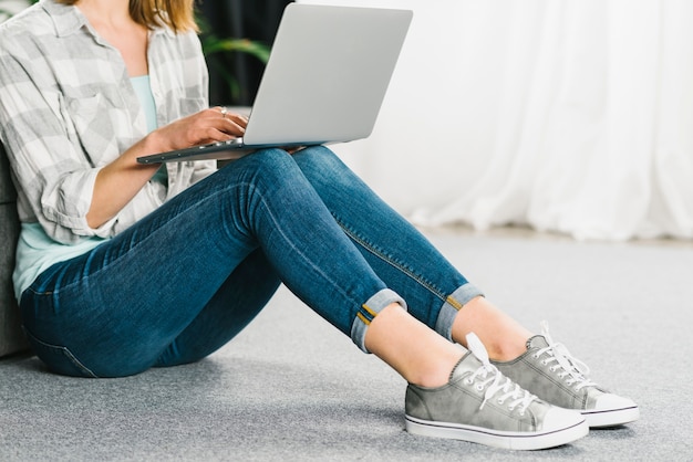 Crop woman using laptop on floor