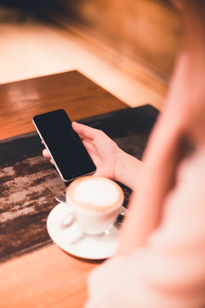 Crop woman using smartphone near coffee