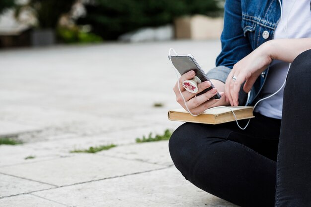 歩道に座っているスマートフォンを使って作物の女性