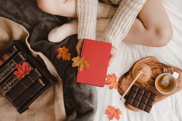 Crop woman with book near tea and leaves