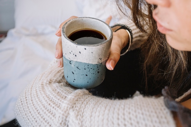 Crop woman with coffee on bed