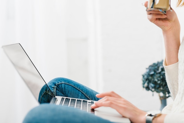 Crop woman with coffee browsing laptop