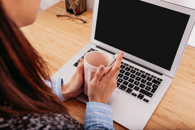 Crop woman with coffee using laptop