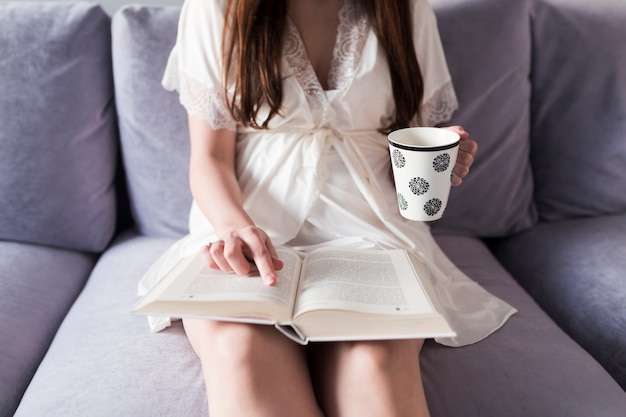 Raccolga la donna con la tazza che legge il romanzo