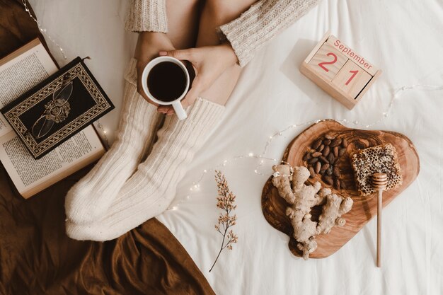 Crop woman with drink near snacks and books