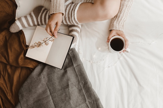 Crop woman with drink putting flower on book