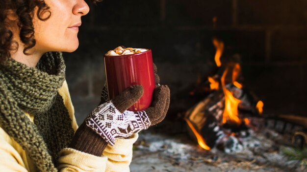 Crop woman with hot beverage near fireplace