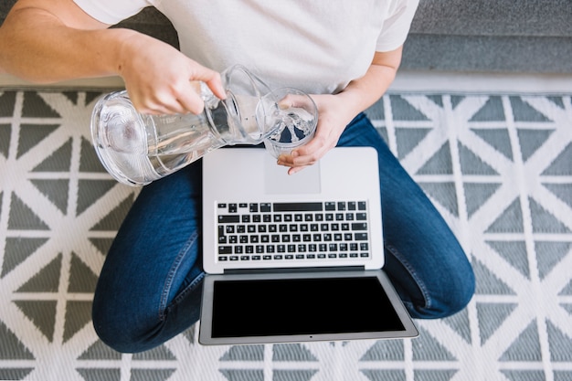 Crop woman with laptop filling glass