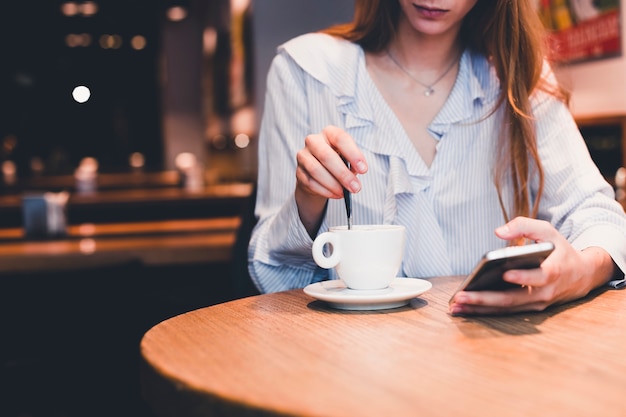 Crop woman with smartphone stirring beverage