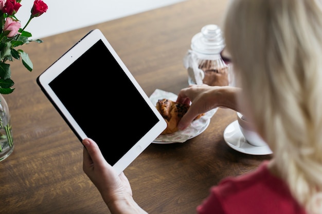 Crop woman with tablet eating bun