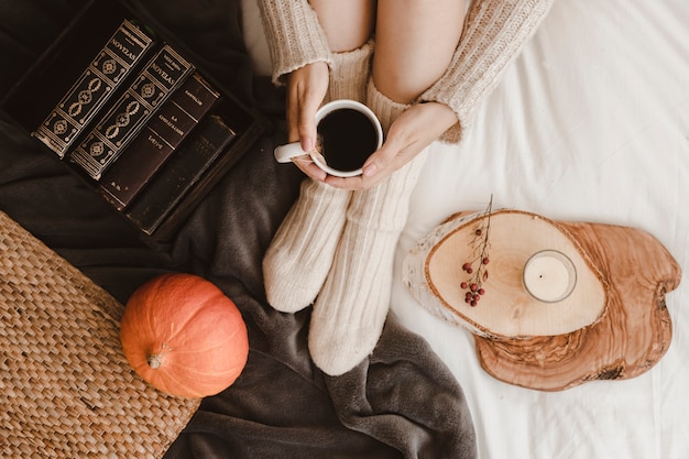 Crop woman with tea near pumpkin and books