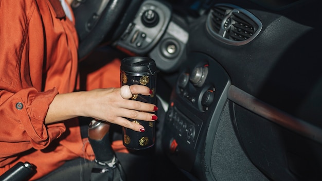 Crop woman with thermos in car