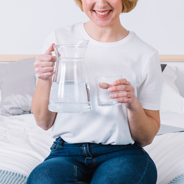 Crop woman with water sitting on bed