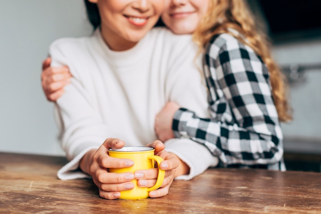 Crop women hugging while sitting at table